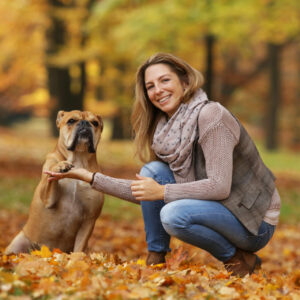 A woman kneels next to a dog while holding one of its paws.